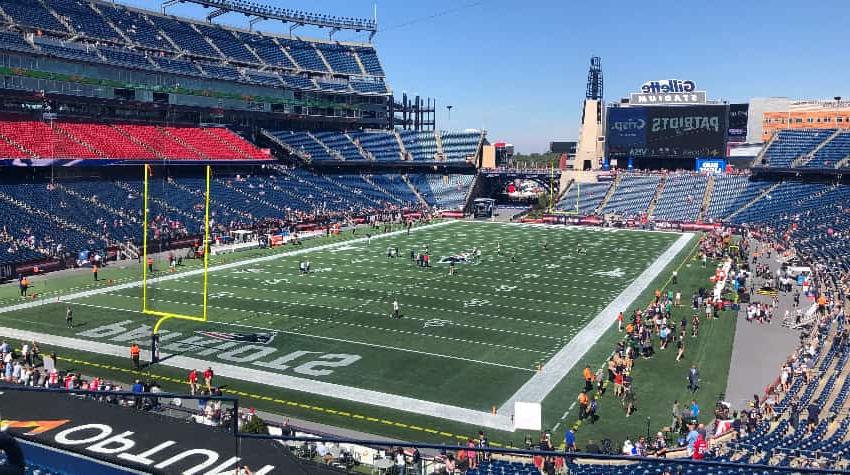 Gillette Stadium on a sunny day, fans and players walking around on the field